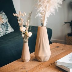 two vases sitting on top of a wooden table filled with flowers and feathers in front of a couch