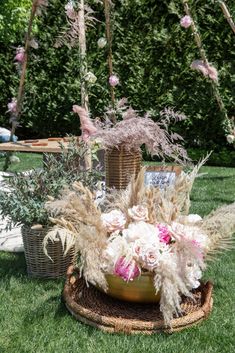 a basket filled with flowers and plants on top of a grass covered field next to trees