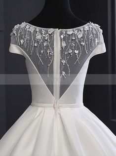 the back of a white wedding dress on a mannequin head stand in front of a black background