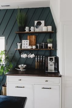 a kitchen with green walls and white cupboards, black counter top and shelves filled with items