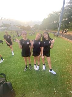 three girls in black shirts and shorts posing for the camera on a field with backpacks