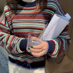 a woman holding a glass and paper in her hand while wearing a colorful striped sweater