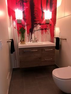 a white toilet sitting in a bathroom next to a sink and a mirror with red paint on it