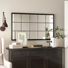 a living room with a mirror, chair and vase on the sideboard in front of it