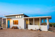 a small white house sitting on top of a dirt field next to a blue door