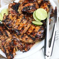 grilled chicken with lime wedges on a white plate next to utensils