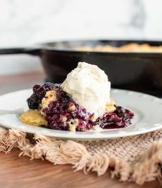 a white plate topped with blueberry cobbler next to a cast iron skillet