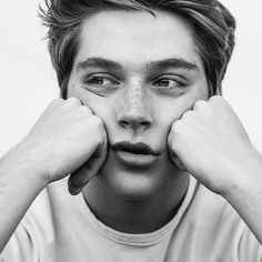 a black and white photo of a young man with his hands on his face looking at the camera