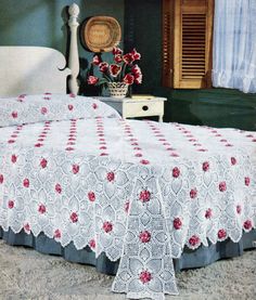 a white bed with red flowers on it in a room next to a dresser and window