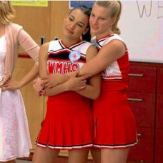 two young women in cheerleader outfits hugging each other while standing next to another woman