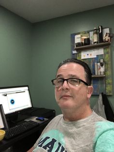 a man sitting in front of a computer desk with a monitor and keyboard on it