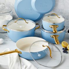 blue pots and pans with gold handles on a white countertop next to lemon slices