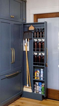 an open cabinet in the middle of a kitchen with brooms and cleaning supplies inside