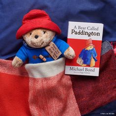 a teddy bear in a red hat and blue shirt is next to a book about paddington