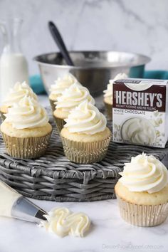 cupcakes with white frosting sitting on a wicker tray next to a box of hershey's milk