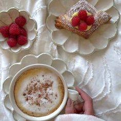 a person holding a cup of coffee in front of some pastries on a plate