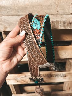 a hand holding a brown and turquoise belt with an elephant design on the bottom, in front of wooden pallets