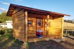 a small wooden cabin with a red door and window on the outside, in front of a grassy field