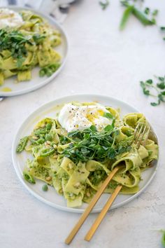 two white plates with pasta and vegetables on them, one has an egg in the middle