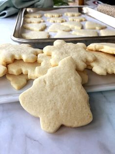 some cookies are on a white plate near a cookie sheet and a pan with christmas tree shaped cookies