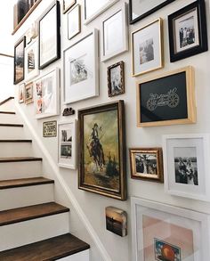 there are many framed pictures on the wall next to the stair case and handrail