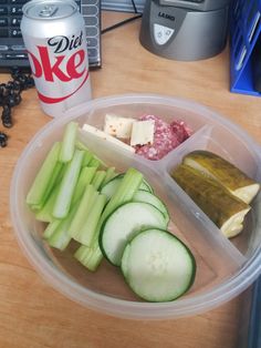 a plastic container filled with cucumbers, cheese and pickles next to a can of diet coke