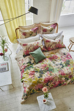 a bed with floral sheets and pillows in a room next to a chair, table and window