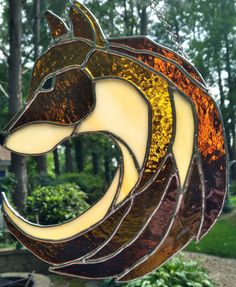 a stained glass wolf head hanging from a chain in front of some bushes and trees