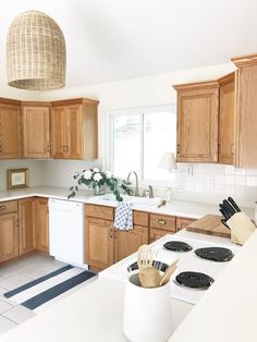 a kitchen with wooden cabinets and white counter tops, an island in the middle has utensils on it