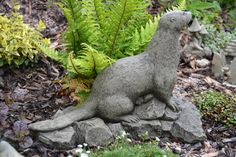 a statue of a dog sitting on top of a rock next to plants and rocks