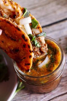 a hand holding up a tortilla in a jar filled with sauce and vegetables