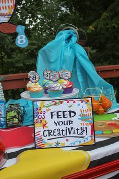 a table topped with lots of cupcakes and cake next to a sign that says feed your creativity