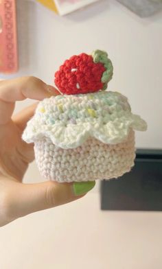 a small crocheted cupcake with a strawberry on top is held up in the air