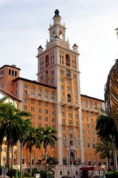 a tall building with a clock on the top and palm trees in front of it