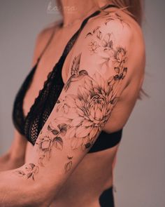 a woman's arm with flowers on it and a black bra - top in the background