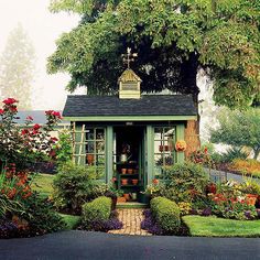 a small green shed sitting in the middle of a lush green yard with lots of flowers