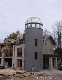 a large gray tower with a glass top in front of a house under construction on a cloudy day