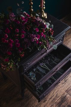 a table with two drawers and flowers on it, next to a candelabra