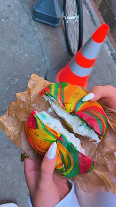 a person holding a colorful doughnut with candy on it and a traffic cone in the background