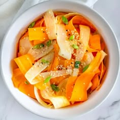 a white bowl filled with sliced carrots and sesame seeds on top of a table