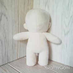 a white teddy bear sitting on top of a wooden floor next to a wall with wood paneling