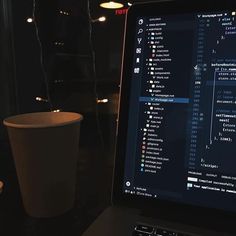 a laptop computer sitting on top of a desk next to a coffee cup and candle