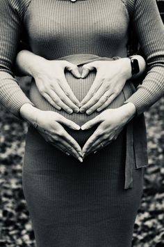 a pregnant woman is holding her stomach in the shape of a heart with both hands