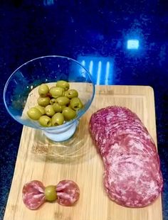 a wooden cutting board with olives and meat on it next to a bowl of green olives