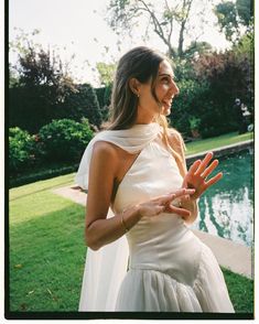 a woman in a white dress is holding out her hands to the side while standing next to a pool