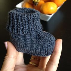 a hand holding up a knitted boot next to a bowl of oranges on a table