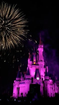 the castle is lit up at night with purple lights and fireworks in the sky above it