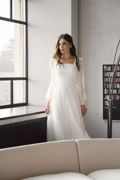 a woman standing in front of a window wearing a white dress with long sleeves and an open back