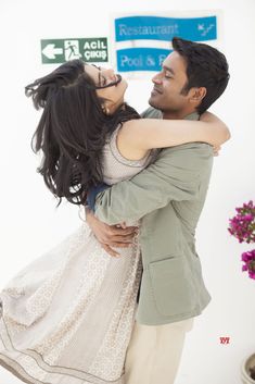 a man and woman hugging each other in front of a sign