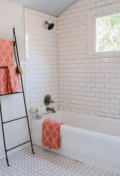 a bathroom with white tile and orange towels on the rack next to the bathtub